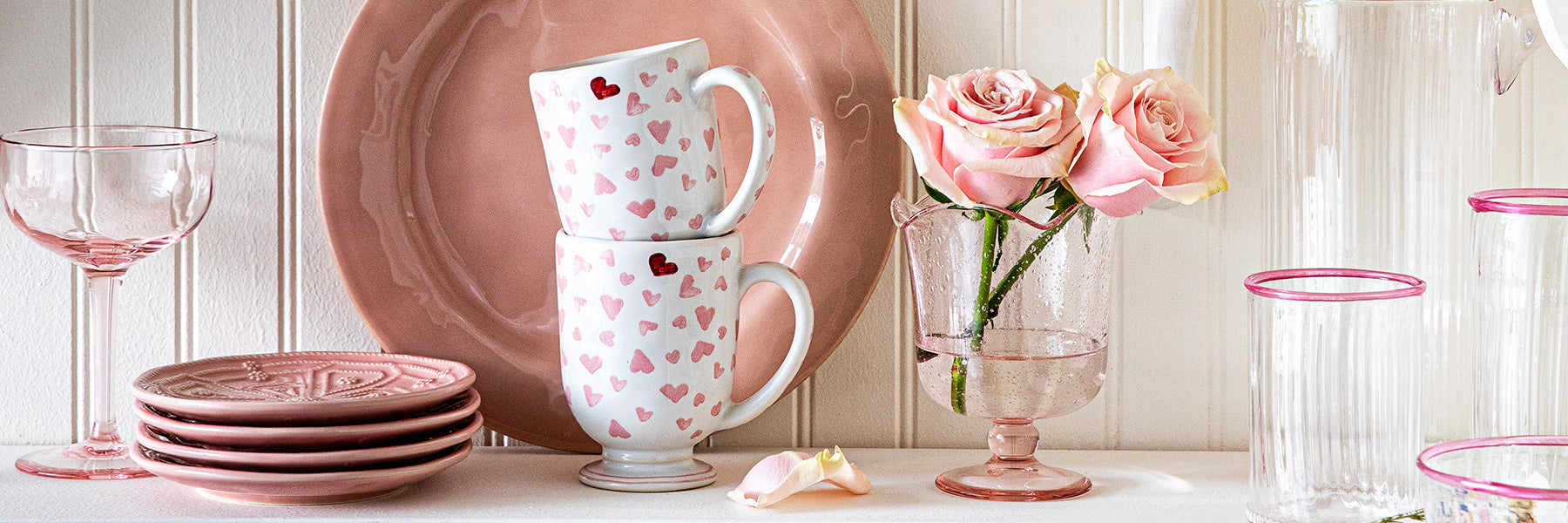 Image featuring pink plates, glassware, and mugs displayed in a cabinet