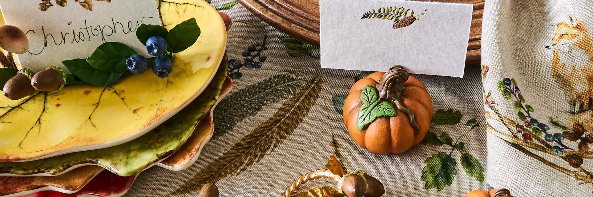 Thanksgiving table setting with pumpkins, place cards, and decorative napkins.