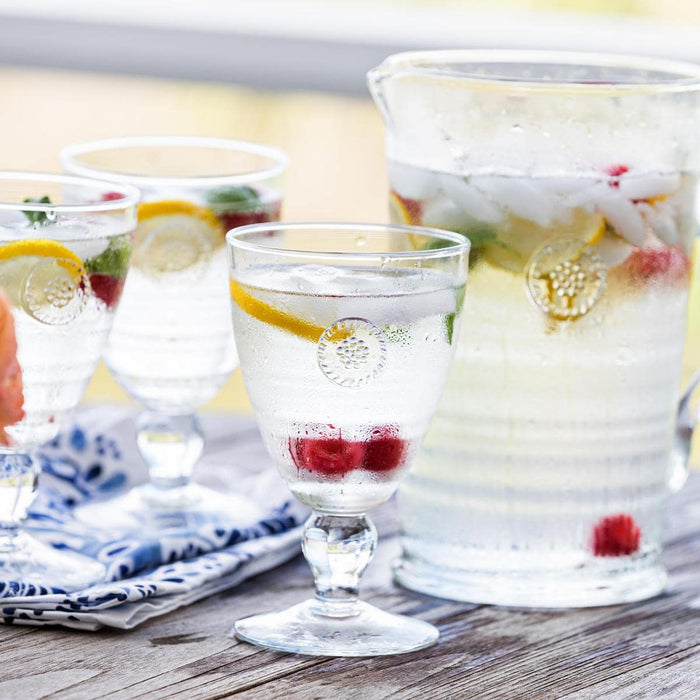 Goblets containing fresh ice water with lemons and raspberries sit on an outdoor table.