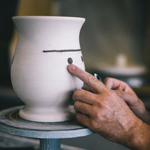 A ceramic vase in it's early form is being shaped by an artist hands.
