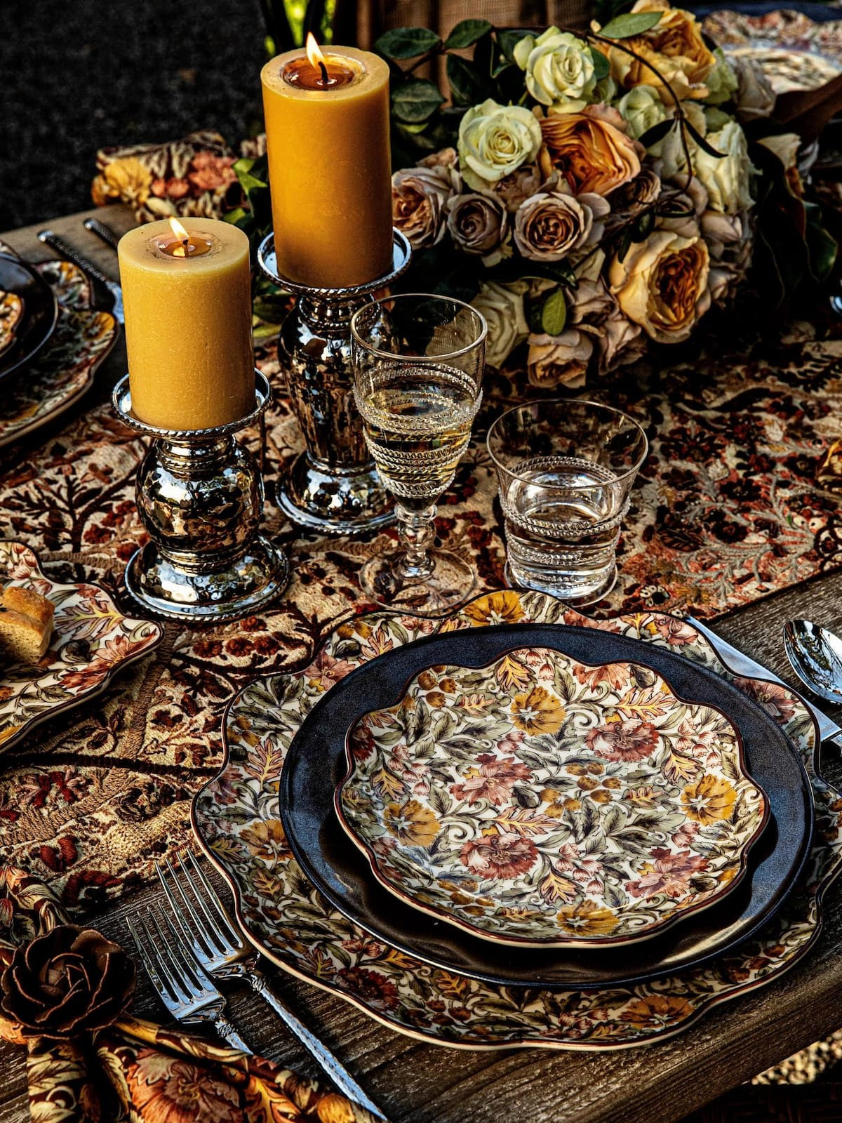 Decorative table setting with candles, glasses, and floral plates on a patterned tablecloth.
