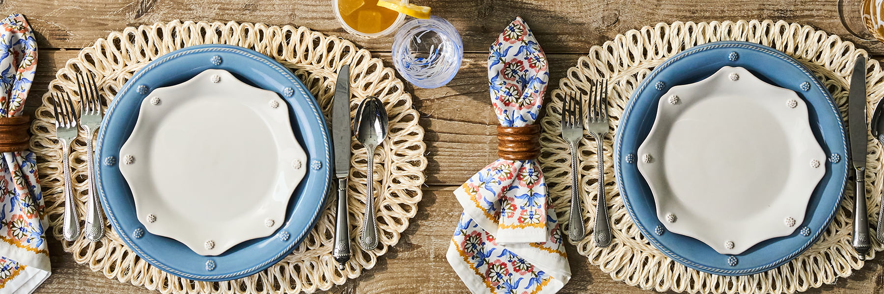 Two chambray ceramic plates on woven placemats, surrounded by cutlery and decorative items on a wooden surface.