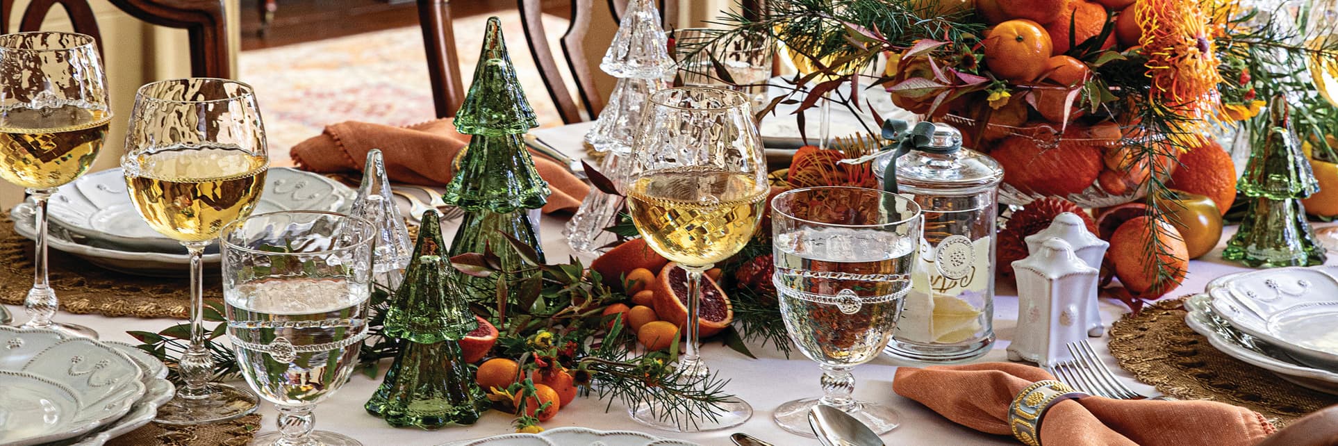 Decorative holiday table setting with place settings, glasses, and a centerpiece.