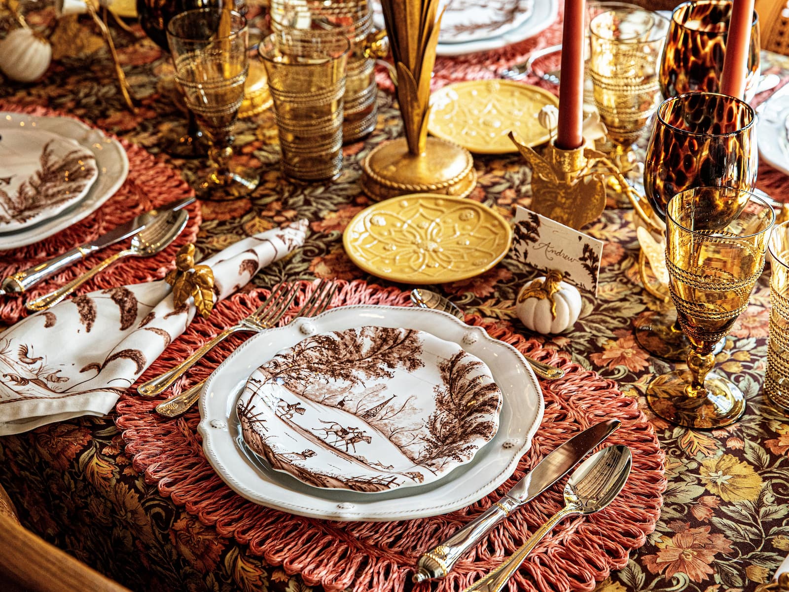 Decorative Thanksgiving table setting with plates, glasses, and place cards on a patterned tablecloth.