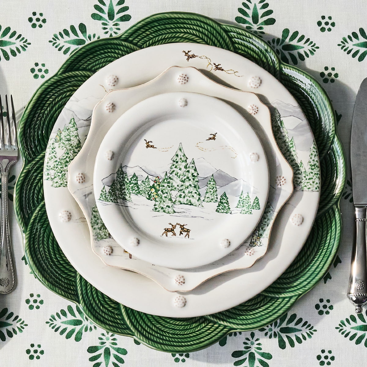 Stack of decorative plates with winter scene design on a patterned tablecloth.