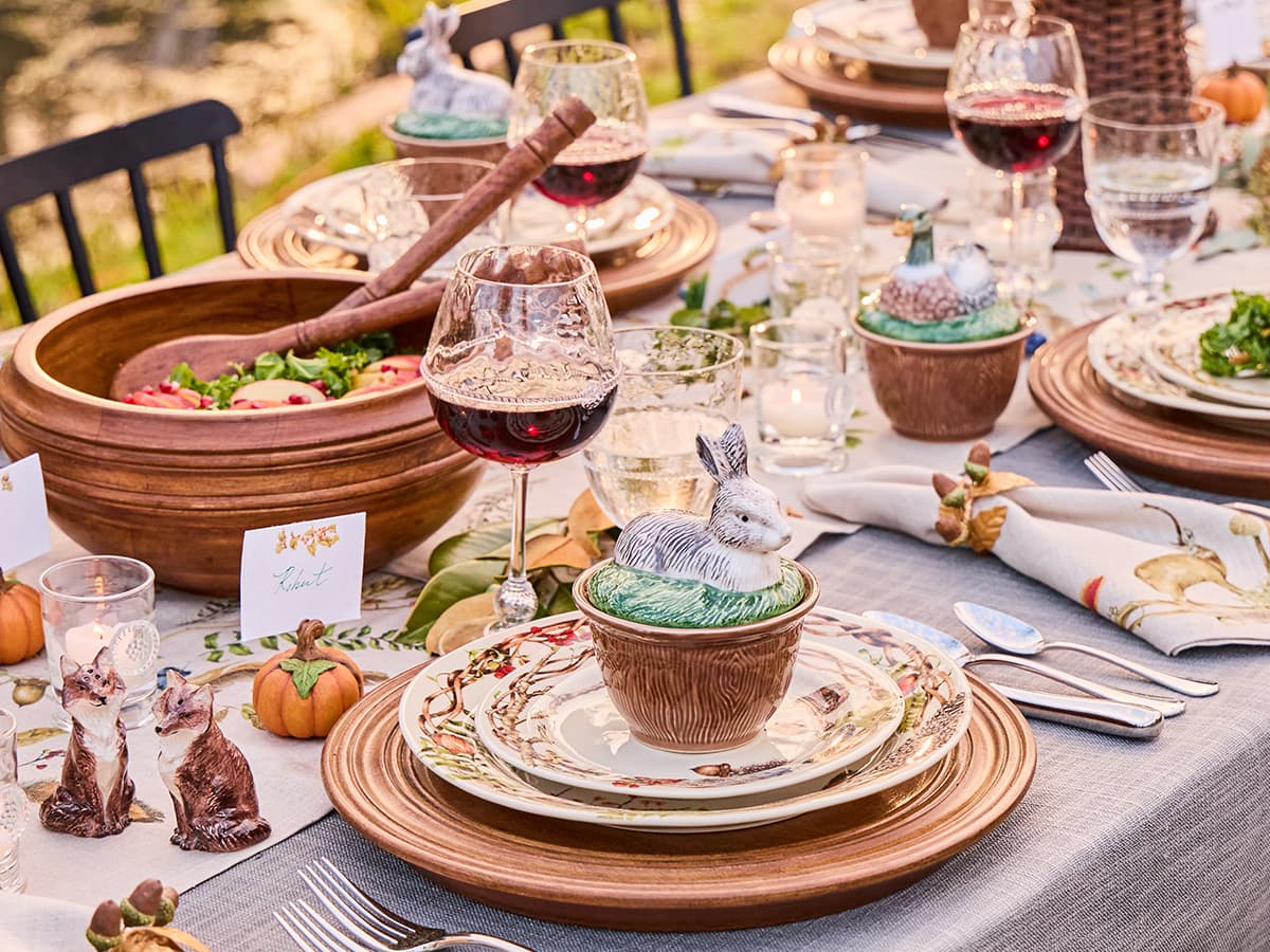 Thanksgiving table setting with wine glasses, plates, and decorative elements outdoors.
