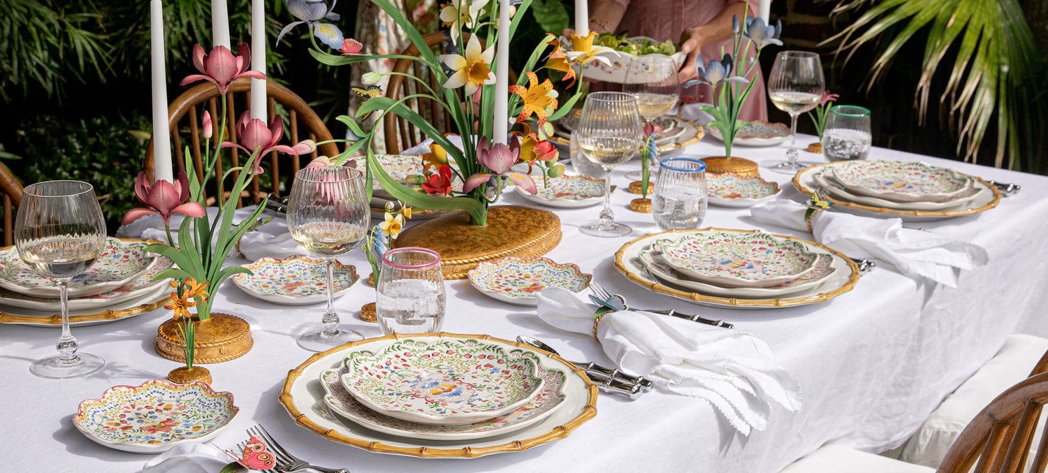 Elegant outdoor dining table setting with floral decorations and patterned plates.