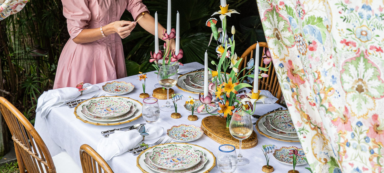 Dining table set with floral decorations and a person in a pink dress in an outdoor setting.