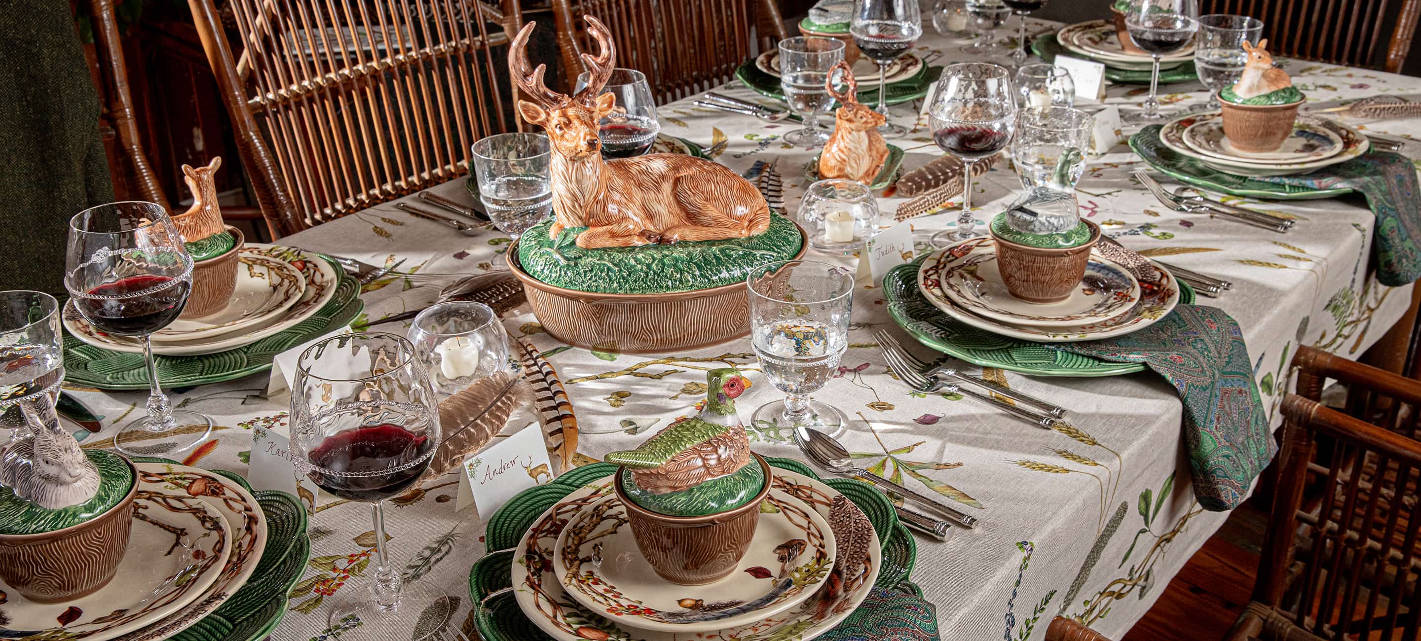 A rustic dining table set with a woodland deer centerpiece, matching green and brown ceramic plates, glassware, and a patterned tablecloth in a warm, rustic interior.