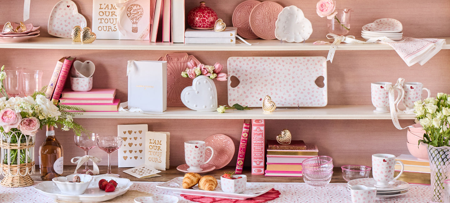Shelf with decorative items including books, vases, and small plants against a pink wall.