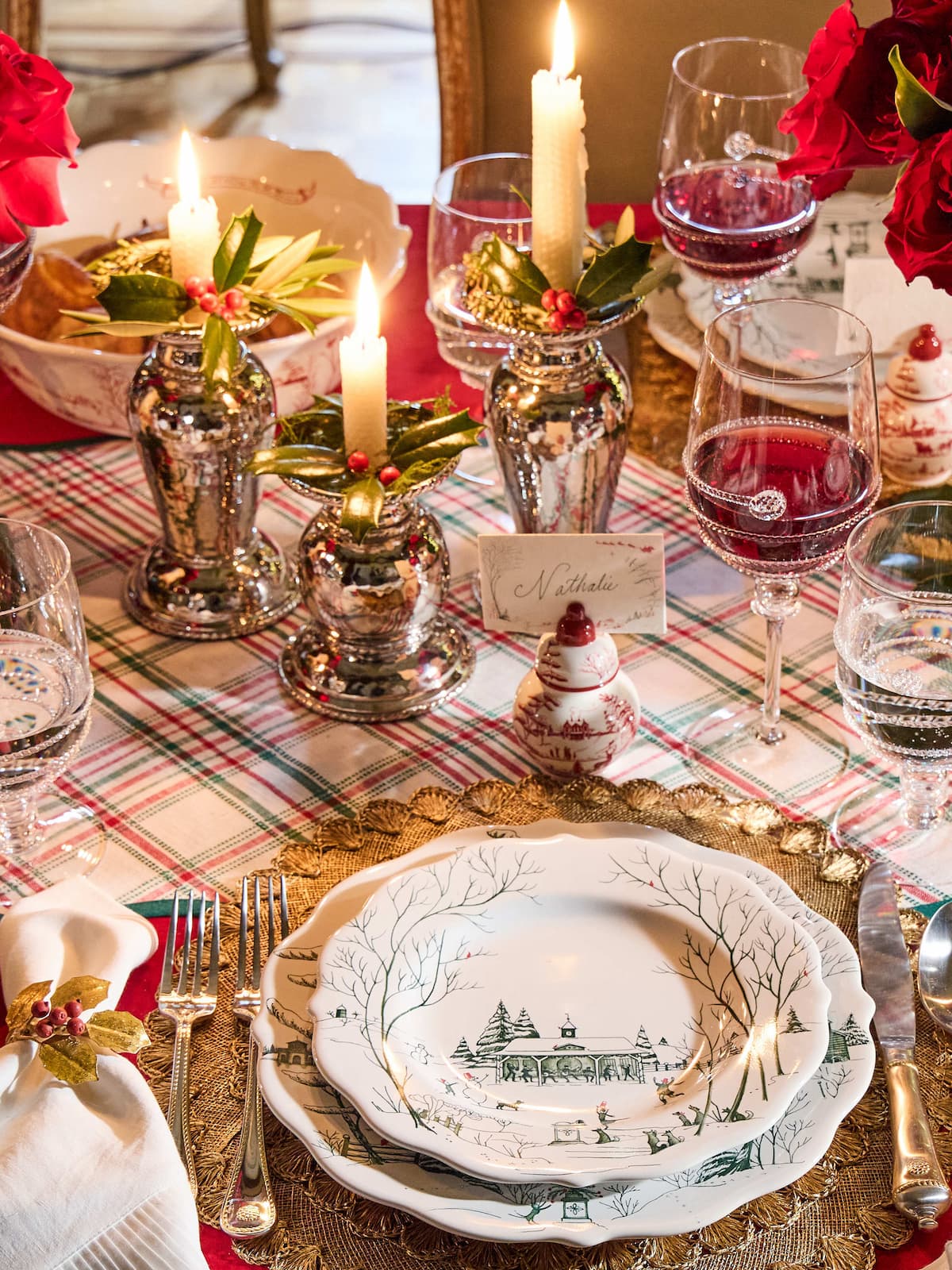 Decorative Christmas table setting with candles, glasses, and a plate with a winter scene.