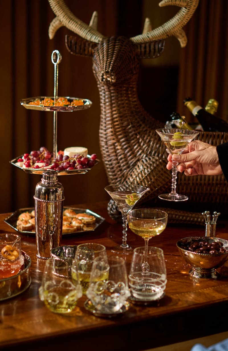 Garnished cocktail with a three-tiered tray and deer head decoration on a wooden table.
