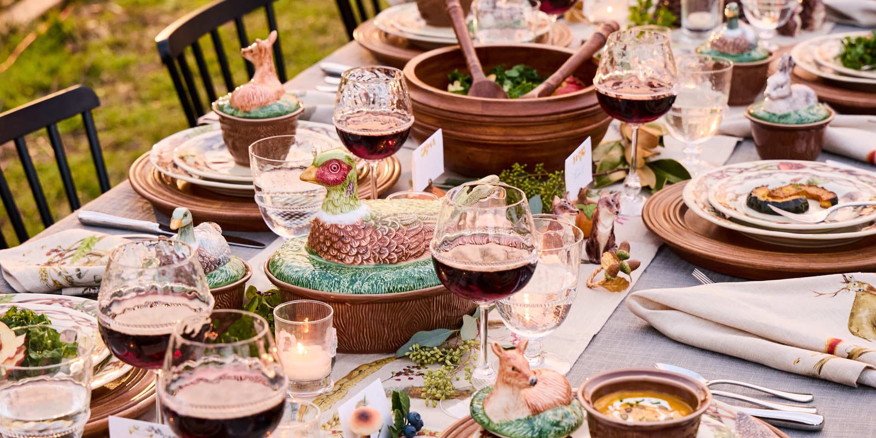 Dining table set for a meal with wine glasses, plates, and decorative elements outdoors.