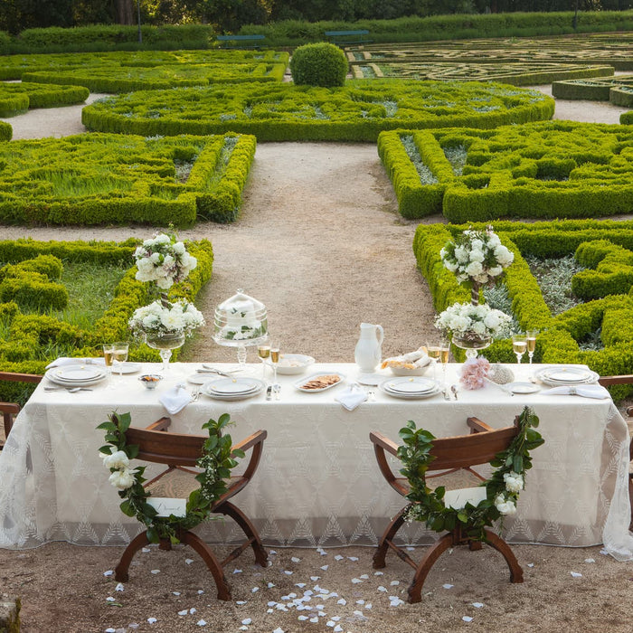 A white table cloth over a long dining table looking out over a green maze garden.