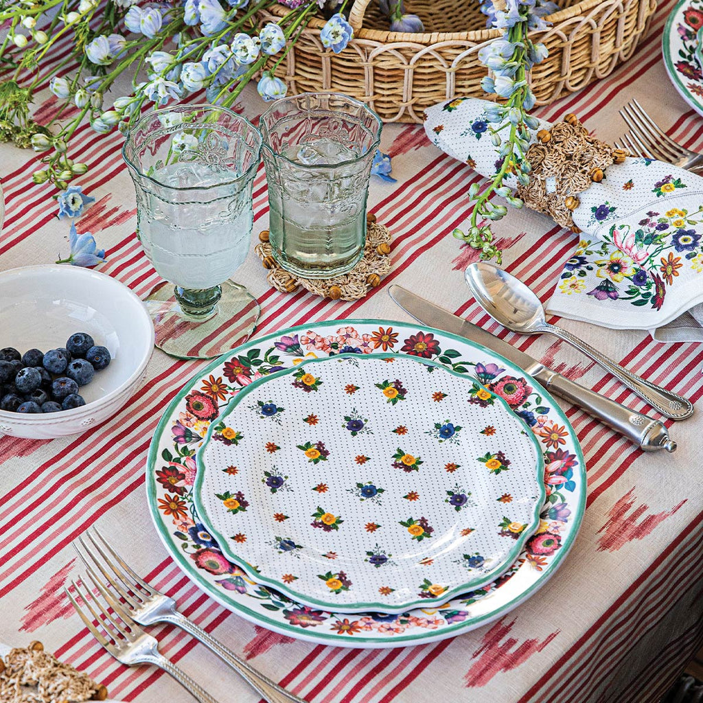 Colorful melamine tableware sits atop a white, red and pink striped tablecloth.