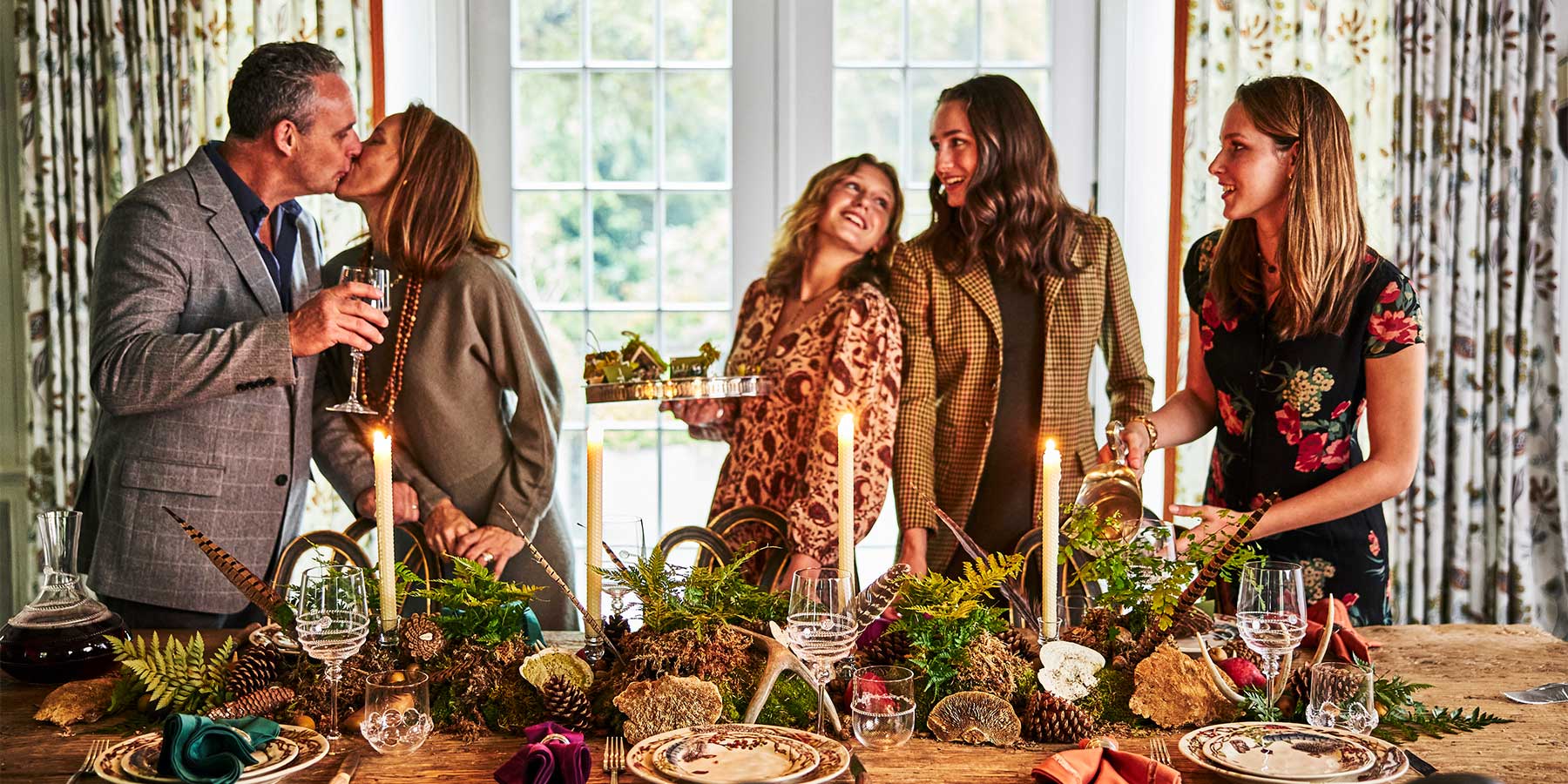 A husband and wife embrace and their children smile as they sand around the Thanksgiving table.
