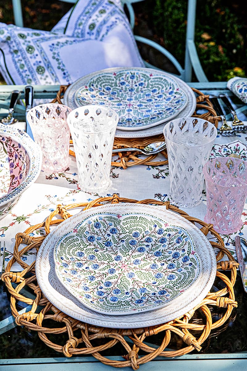 Villa Seville plates stacked on Le Panier whitewash plates and rattan placemats on an outdoor table
