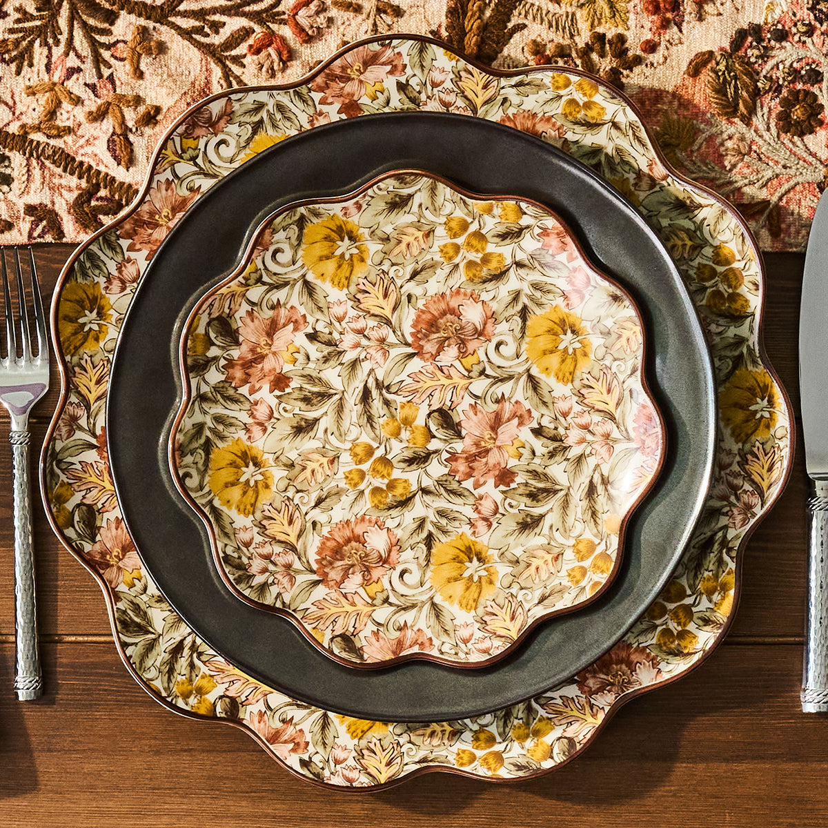Decorative floral plate on a wooden table with a patterned tablecloth.