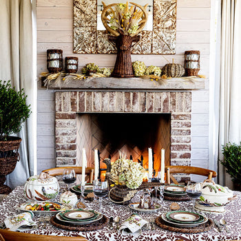A Thanksgiving table is set in front of a warm fireplace.