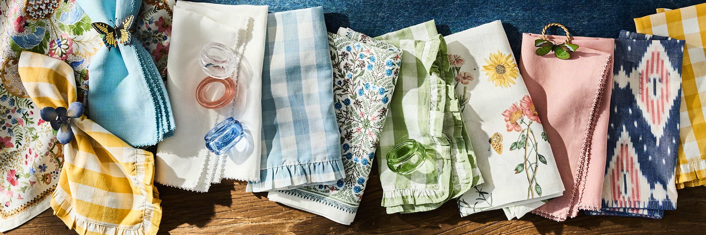 Variety of Juliska placemats and napkins lined up on a green tablecloth