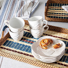 White ceramic cups and plates on a woven placemat with pastries.