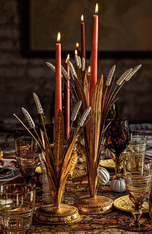 Decorative candle holder with red candles on a table setting with glasses and plates.