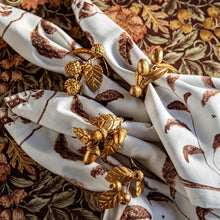 Gold leaf-shaped earrings on a white fabric with brown leaf patterns against a floral background