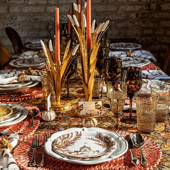 Decorative table setting with gold candle holder, plates, and glasses on a brick wall background.