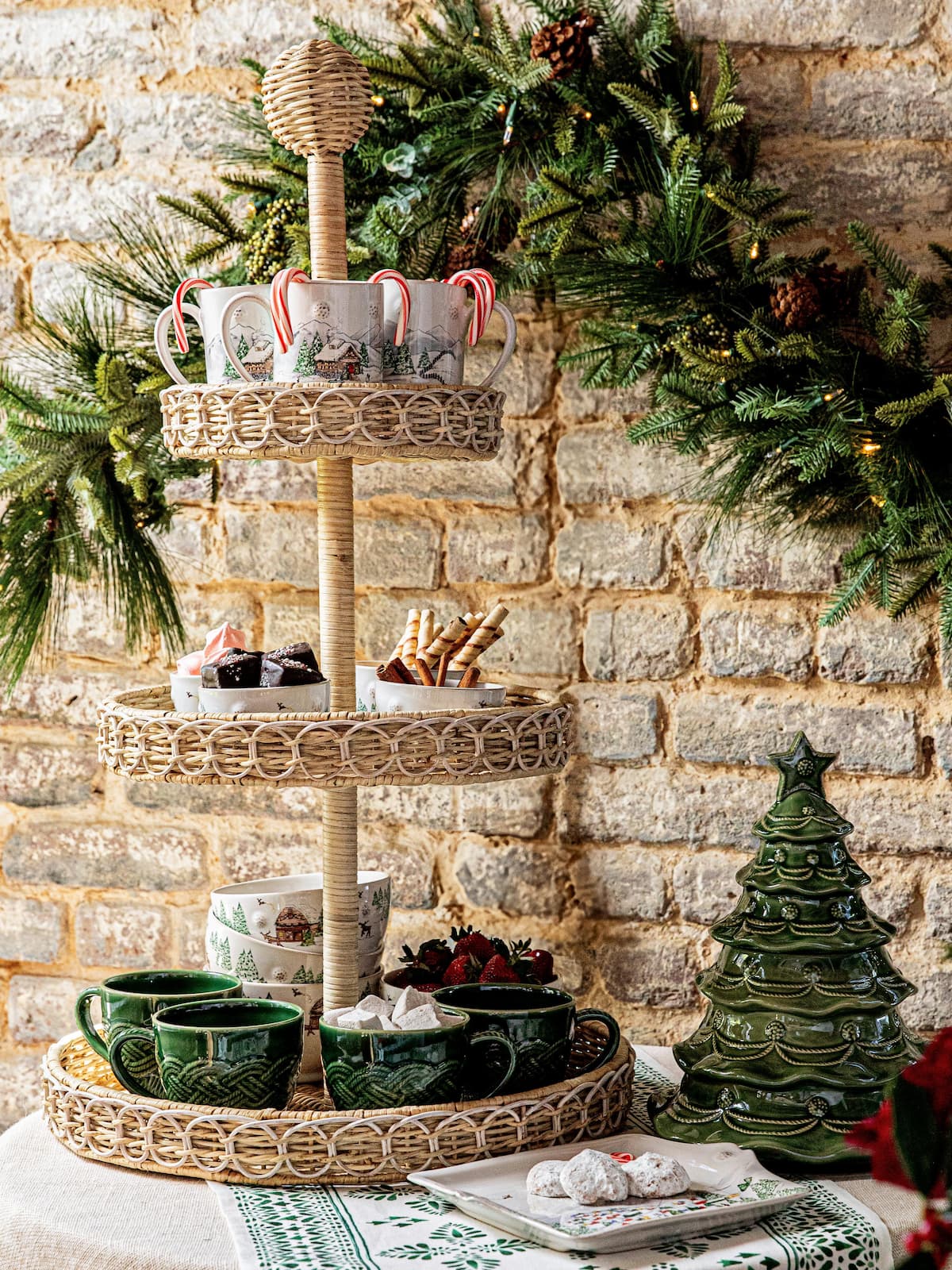 Three-tiered wicker tray with Christmas-themed items against a stone wall.