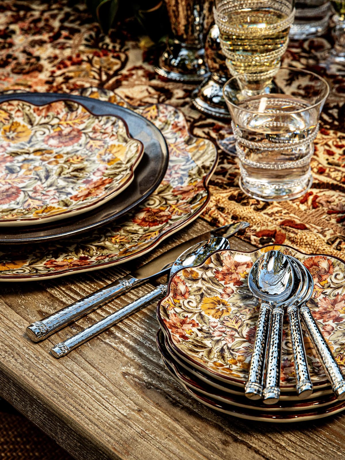 Dinner table setting with pizza, silverware, and glasses on a patterned tablecloth.