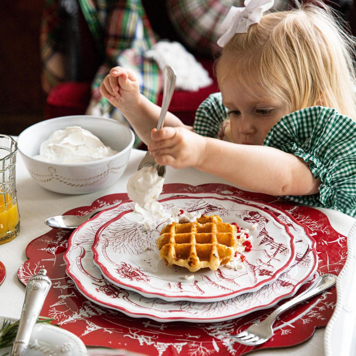 A young girl puts whip cream on her waffle.