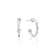 A pair of silver hoop earrings with textured hammered finishes and small floral details at the top and bottom, shown on a clean white background with a soft reflection.