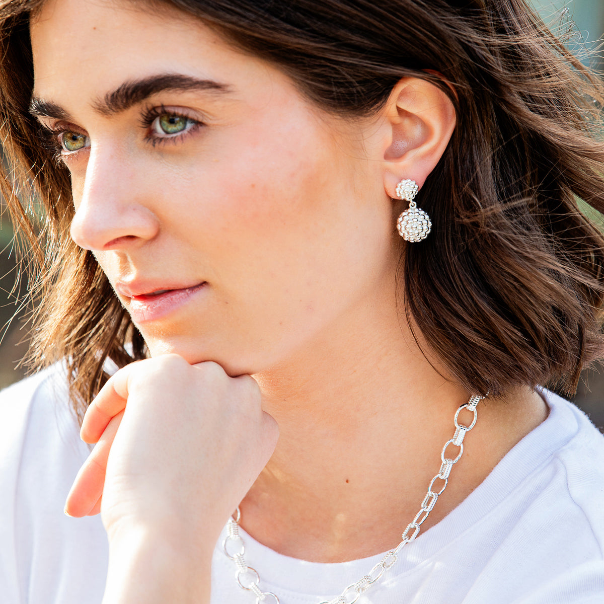 A close-up lifestyle shot of a woman wearing a silver-toned dangle earring with a textured, flower-like drop and a matching silver chain necklace.