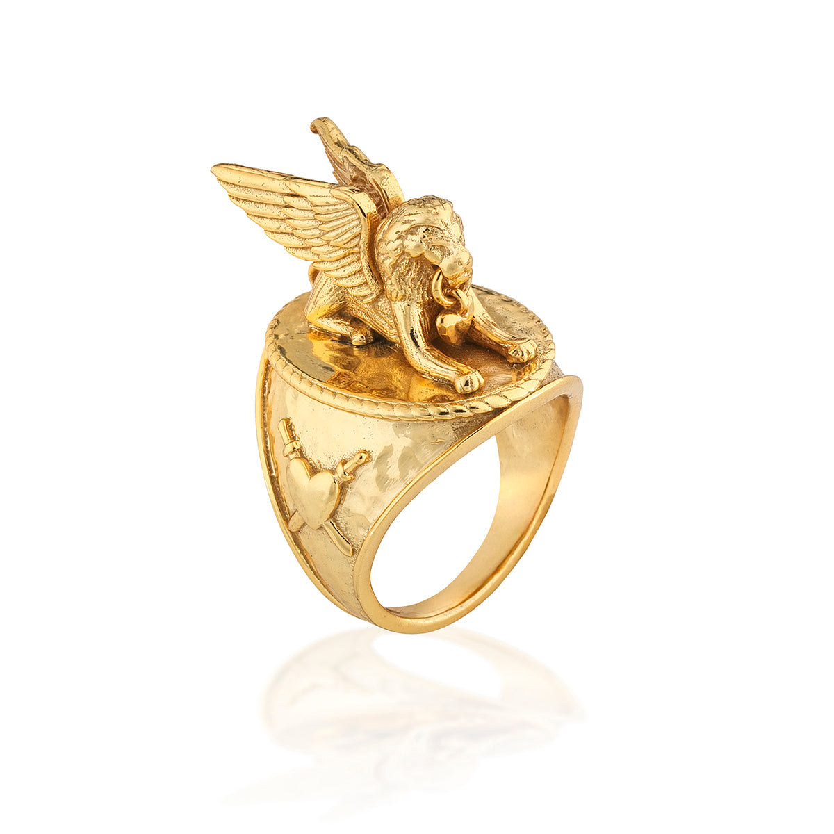 A gold ring featuring a sculpted winged lion on a polished band with engraved details, shown on a white background with a soft reflection.