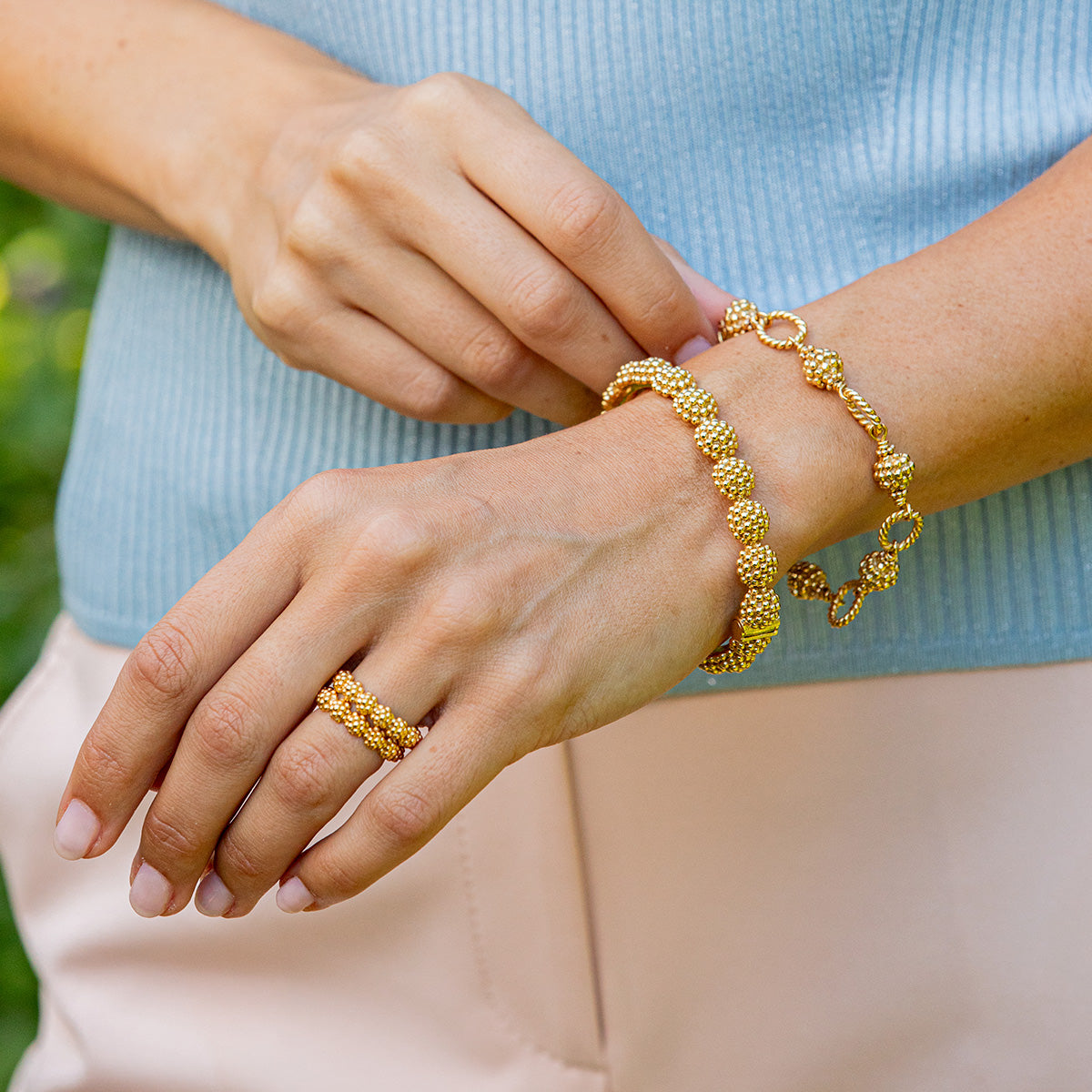 Person wearing gold bracelets and ring on a blurred natural background