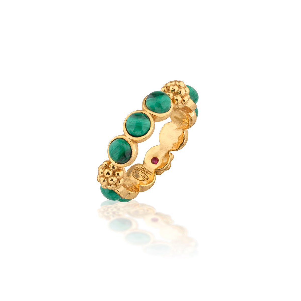 A gold band ring featuring oval green malachite stones, textured gold beads, and a small round red gemstone, shown on a white background with a soft reflection.