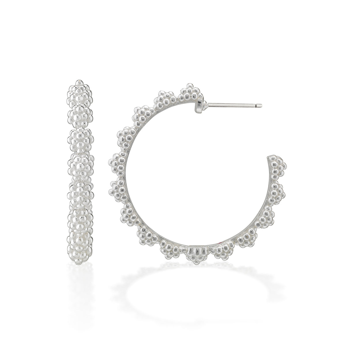 A pair of silver hoop earrings with a textured, beaded floral border, shown on a clean white background with a soft reflection.