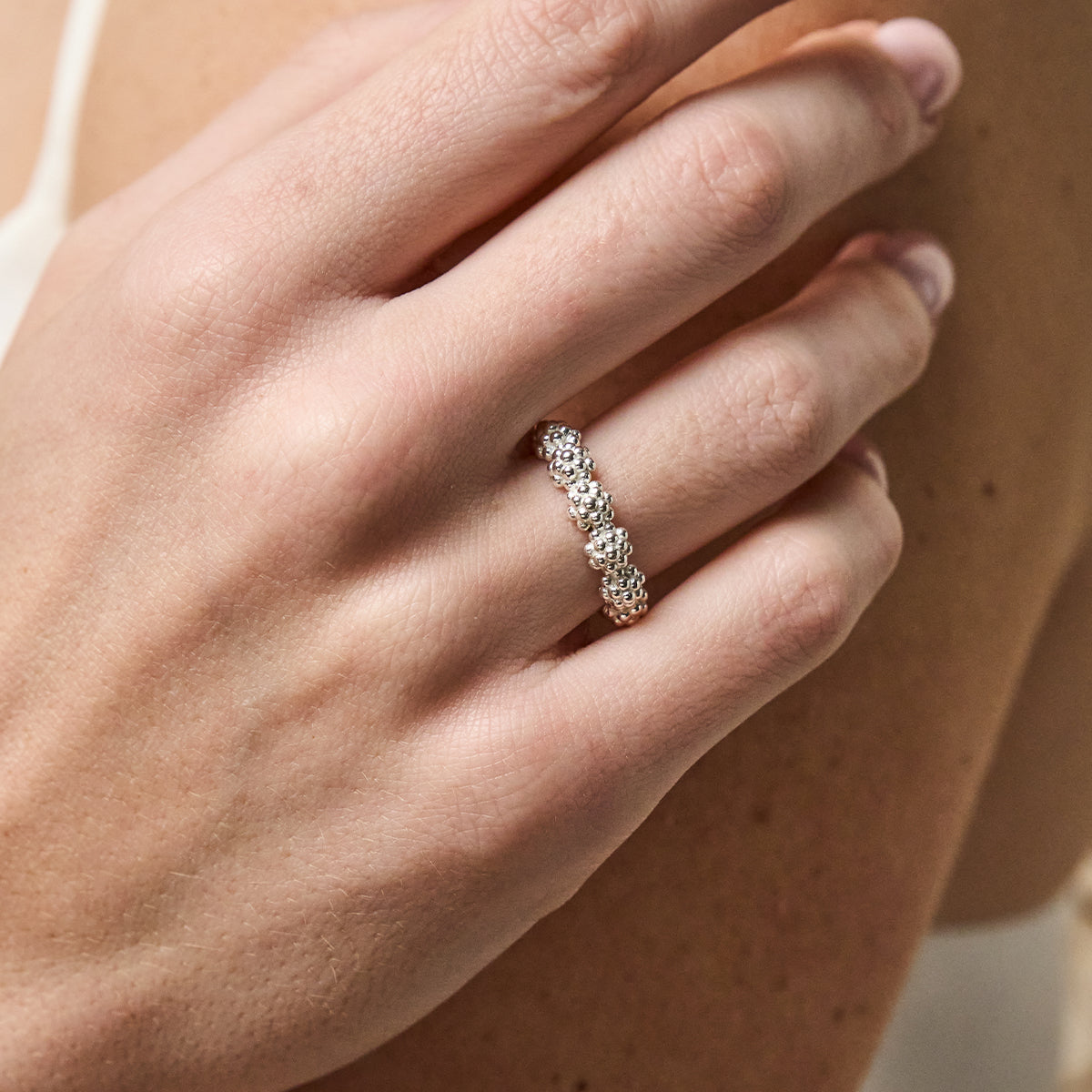 A close-up of a hand wearing a silver band ring set with small clear stones, shown against skin tones.