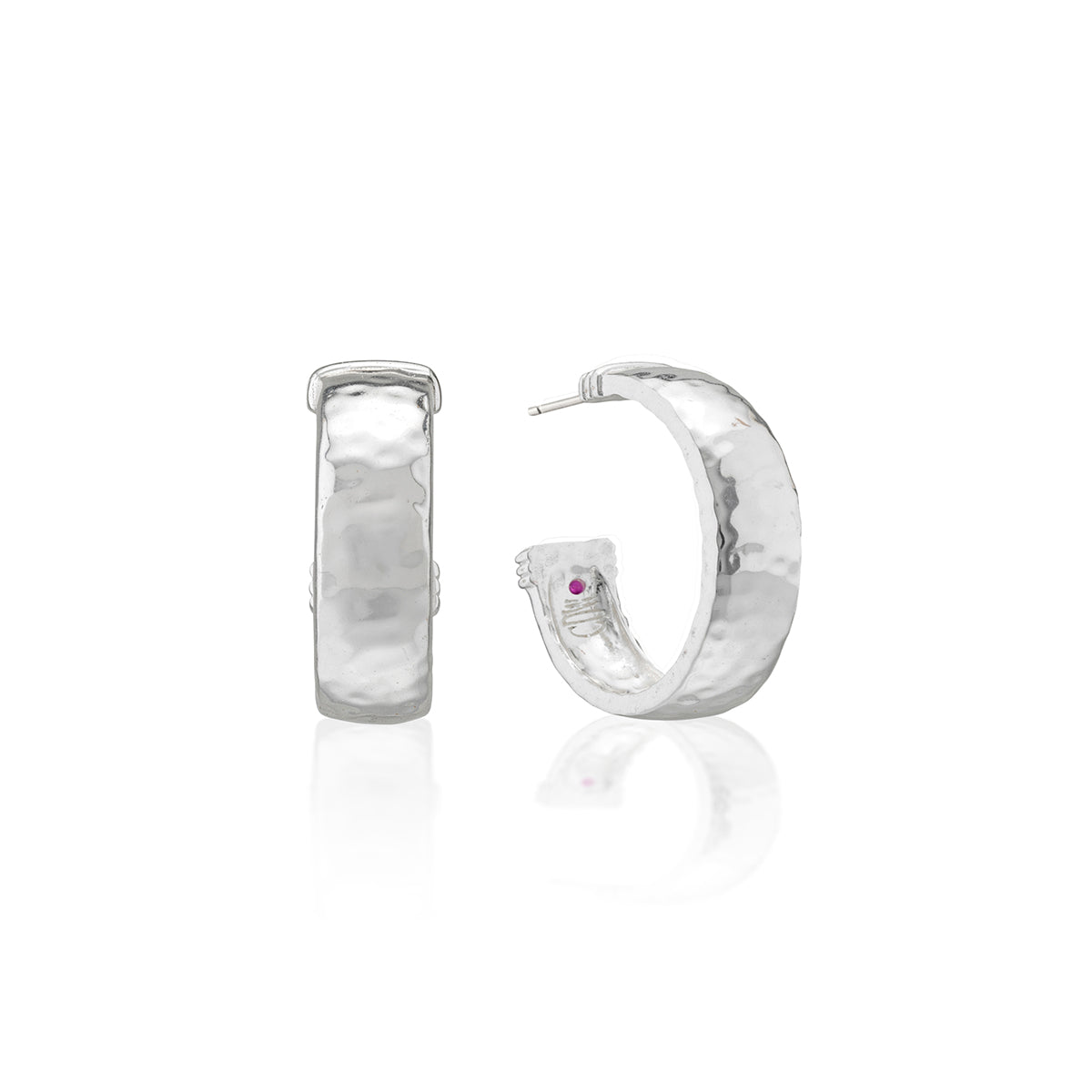 A pair of hammered silver hoop earrings, one shown from the front and the other from the side with a small purple gemstone accent, on a white background with a soft reflection.