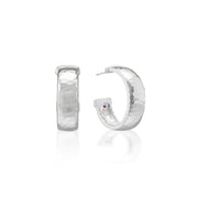 A pair of hammered silver hoop earrings, one shown from the front and the other from the side with a small purple gemstone accent, on a white background with a soft reflection.