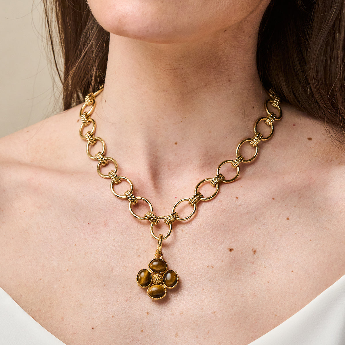 A close-up of a model wearing a gold chain necklace with a pendant made of five polished brown tiger's eye stones.