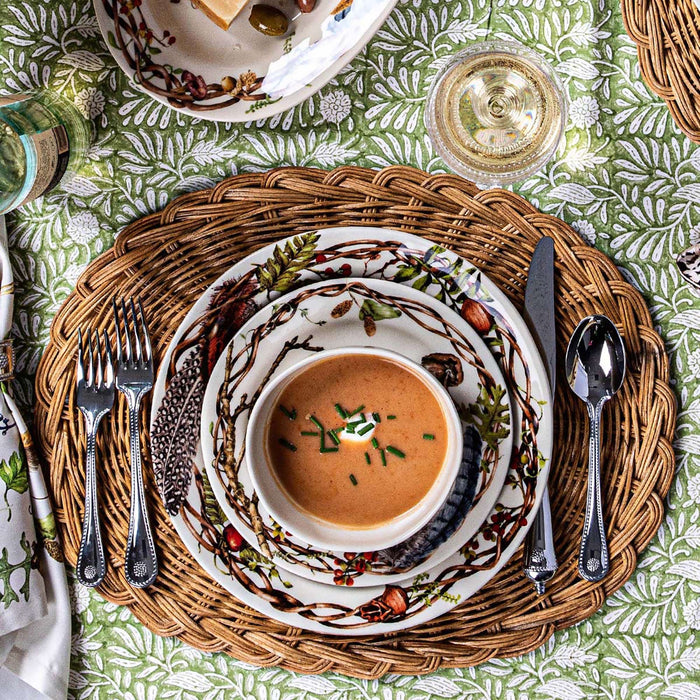 Dinner setting with soup, bread, and cutlery on a patterned tablecloth