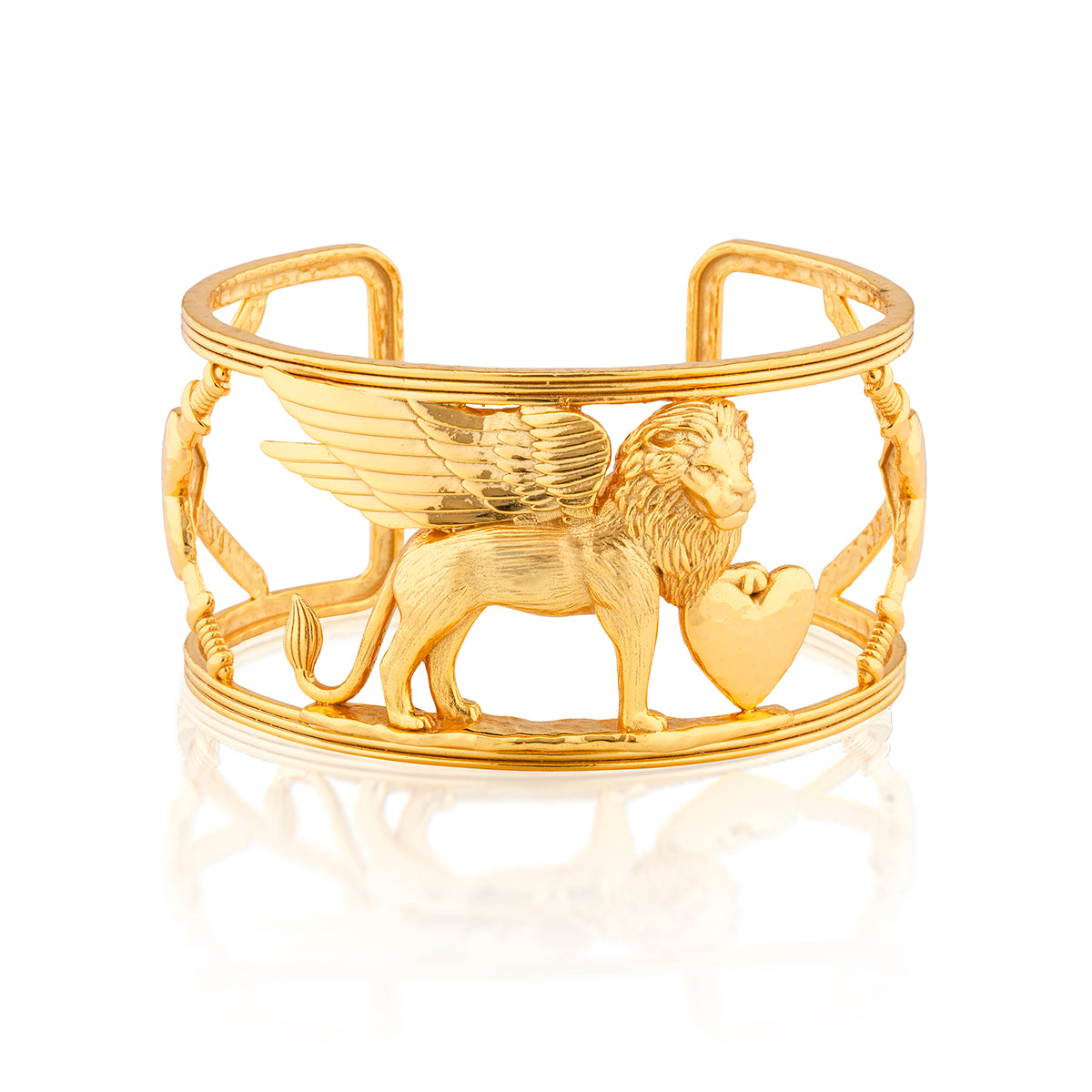 A gold-tone cuff bracelet featuring a winged lion holding a heart, with decorative chain-like side details, shown on a clean white background with a soft reflection below.