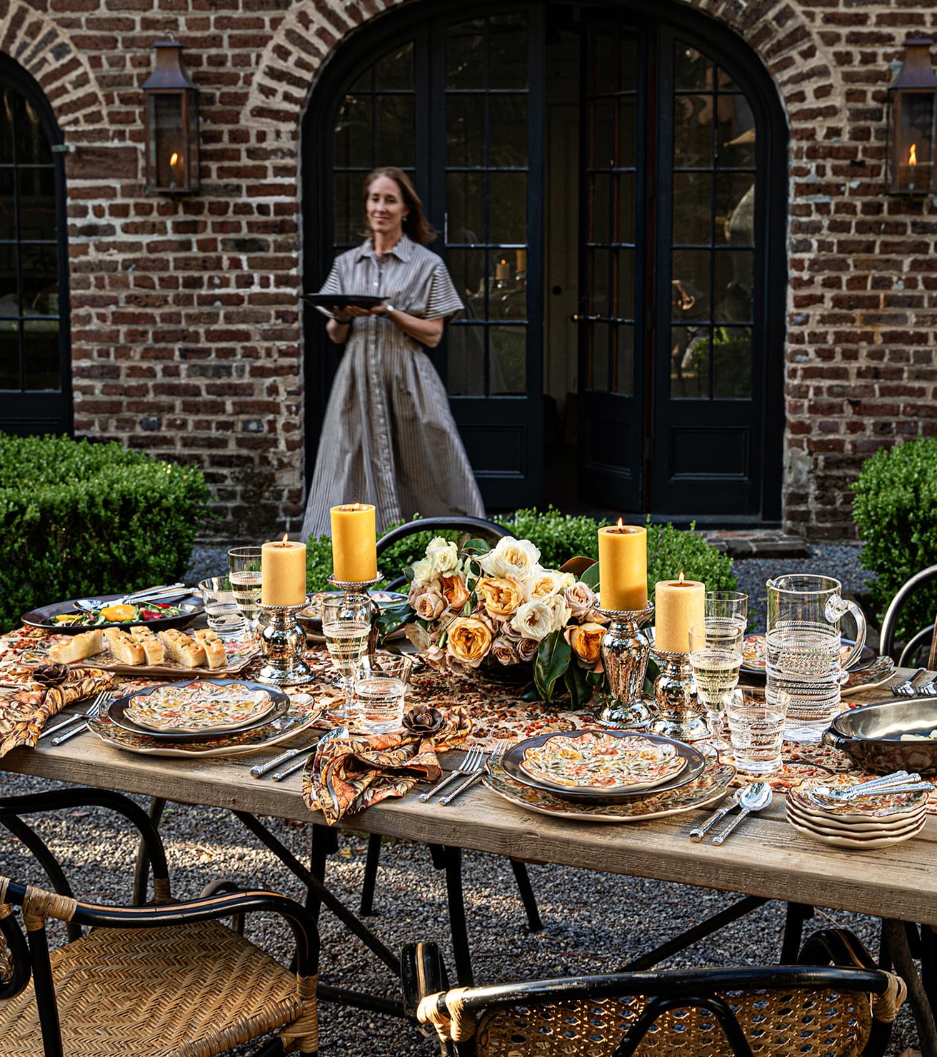Woman standing behind a beautifully set outdoor dining table with candles and flowers.