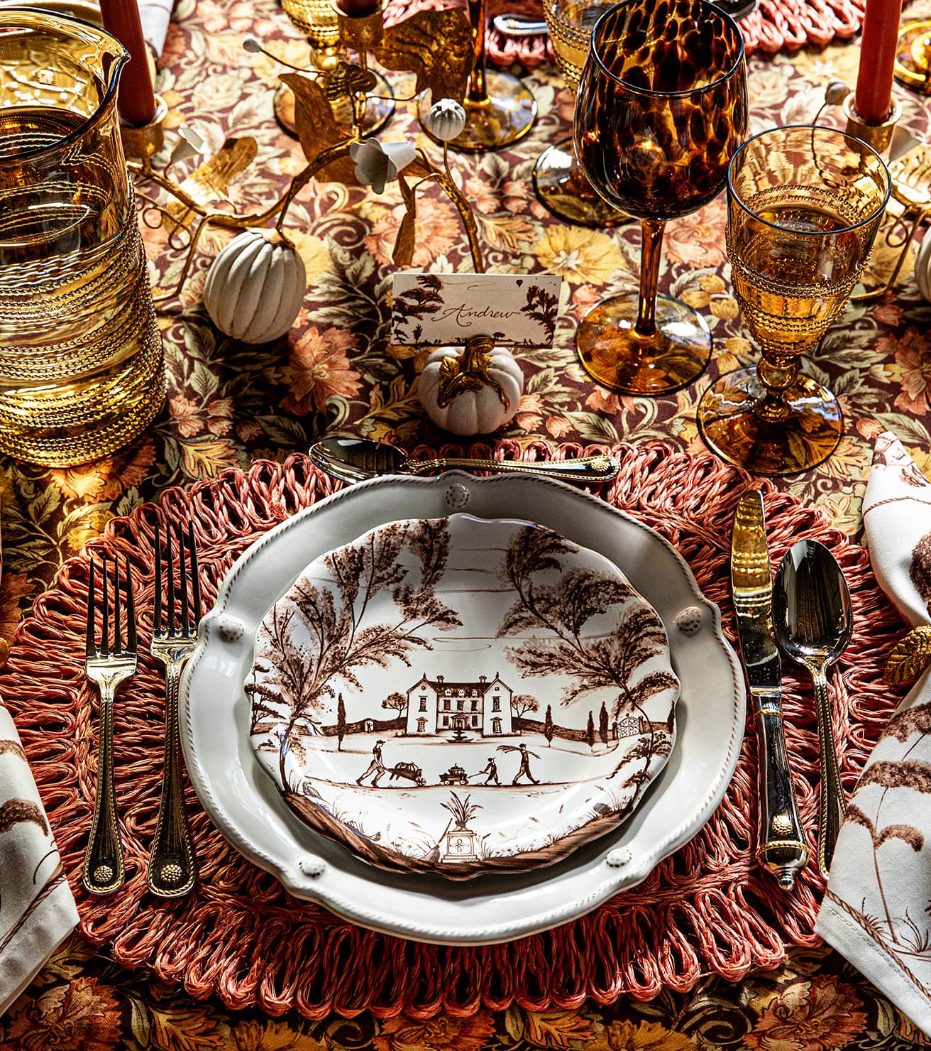 Decorative table setting with vintage-style plates, glasses, and cutlery on a patterned tablecloth.