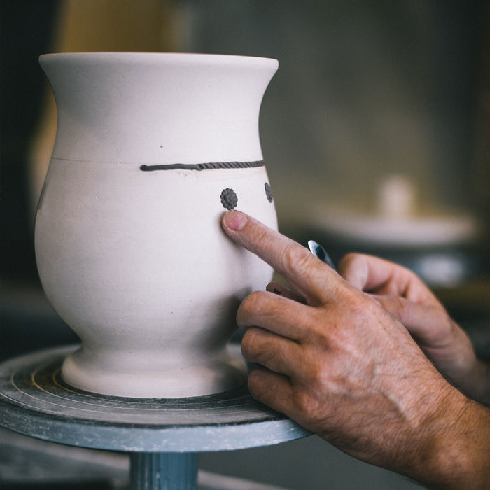 A ceramic vase in it's early form is being shaped by an artist hands.