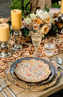 A charger, dinner plate and salad plate are stacked on a outdoor wooden table.