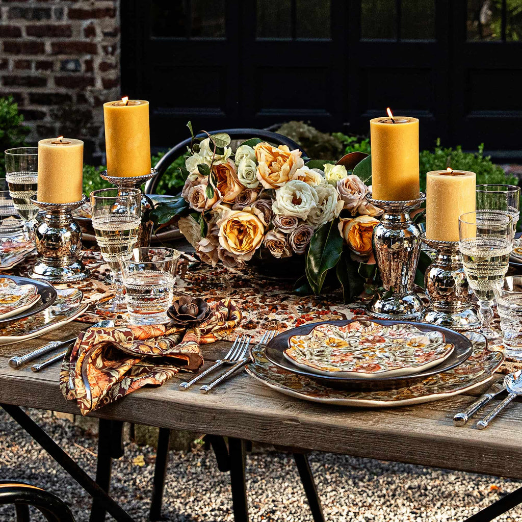 Decorative table setting with candles, flowers, and plates outdoors.