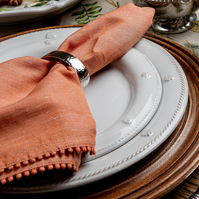 Napkin folded on a white plate with a wooden charger, set on a table.