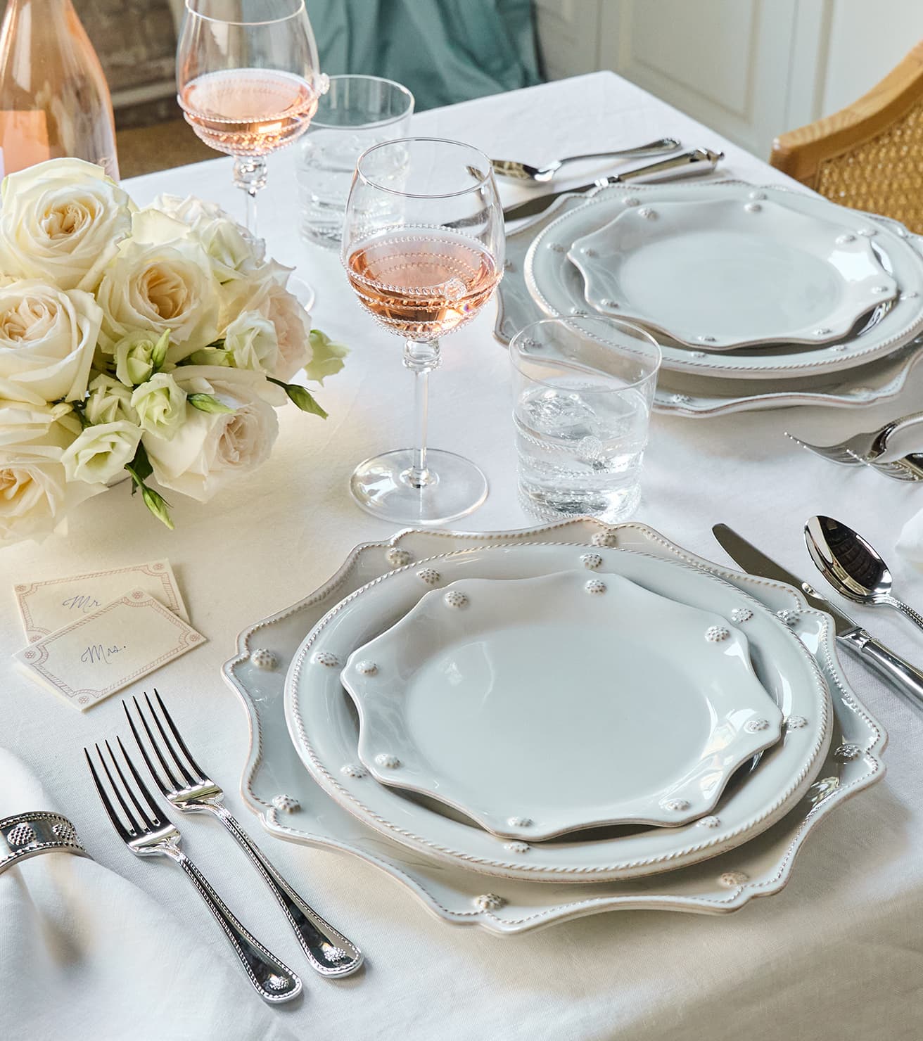 Elegant table setting with white plates, silverware, and floral arrangement on a white tablecloth.